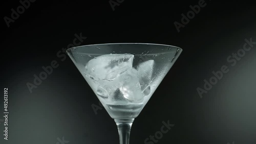 Putting ice cubes in a empty martini glass filling up with absinthe isolated on black background photo