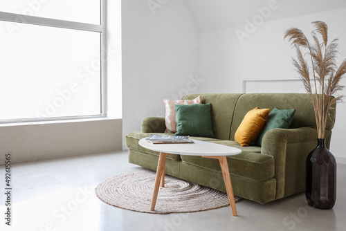 Modern table, sofa and vase with reed flowers in interior of light room