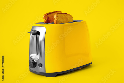 Modern toaster with bread slices on yellow background