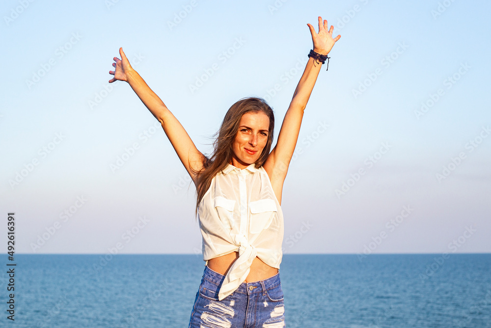 Smiling young woman with raised hands on the background of the sea. Smiling young woman with raised hands on the background of the sea.