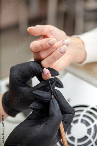 Manicure master, working in the beauty salon covering nails of female client with gel polish