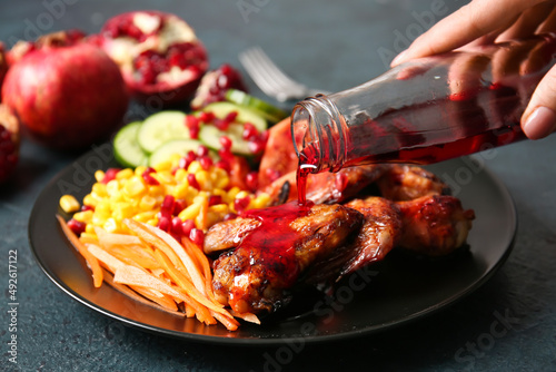 Woman pouring pomegranate molasses onto roasted chicken wings on black background photo