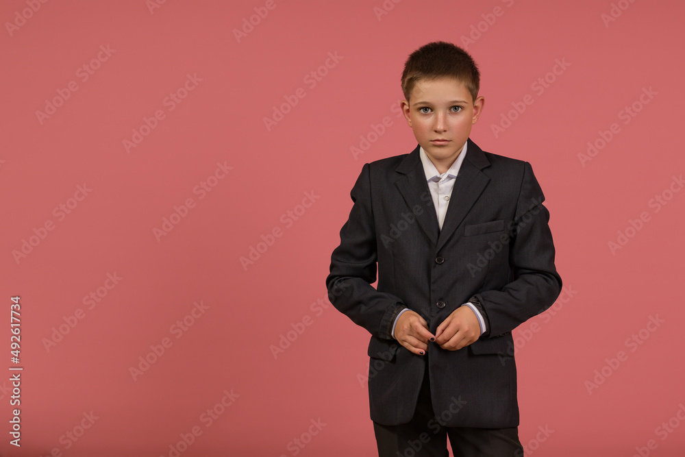 schoolboy buttoning his jacket on a suit on a pink background with copy space schoolboy buttoning his jacket on a suit on a pink background with copy space