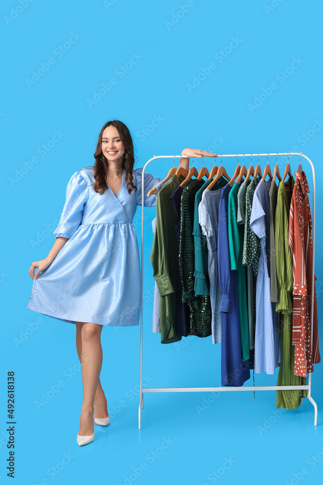 Beautiful young girl near rack with clothes for high school prom on blue background Beautiful young girl near rack with clothes for high school prom on blue background