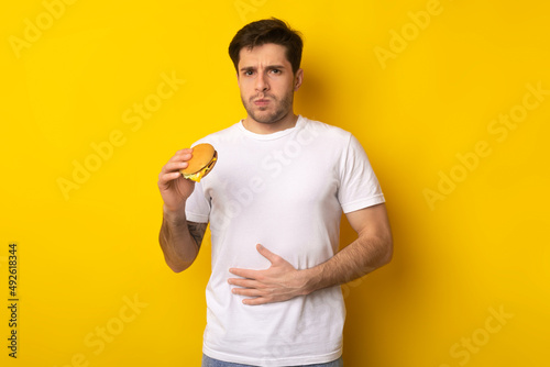 Sad Young Guy Holding Burger Suffering From Stomachache