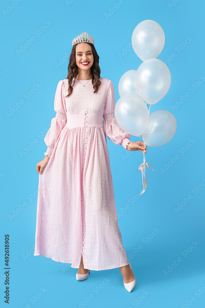 Beautiful young woman in stylish dress and tiara holding balloons on blue background Beautiful young woman in stylish dress and tiara holding balloons on blue background