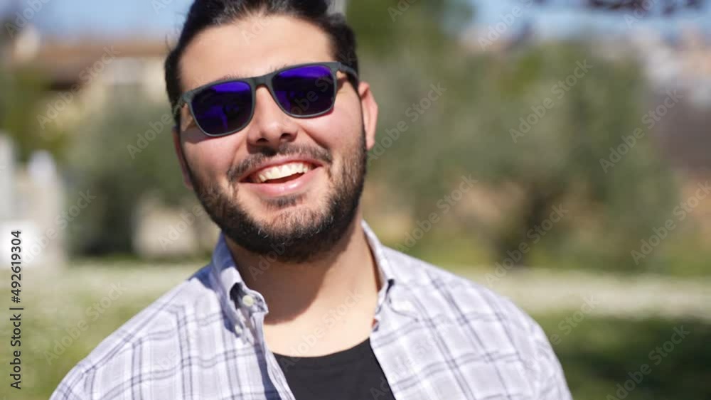 Portrait of an attractive happy bearded casual guy with sunglasses and a checked shirt looking at camera outside. Portrait of an attractive happy bearded casual guy with sunglasses and a checked shirt looking at camera outside.