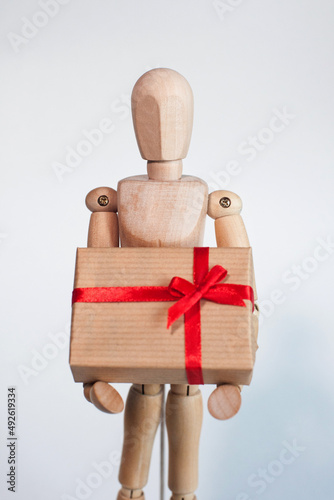 A wooden man holds a box in his hands on a light background