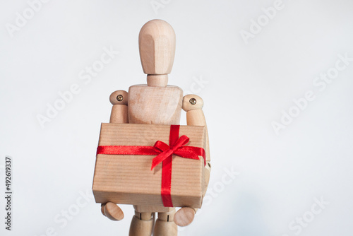 A wooden man holds a box in his hands on a light background
