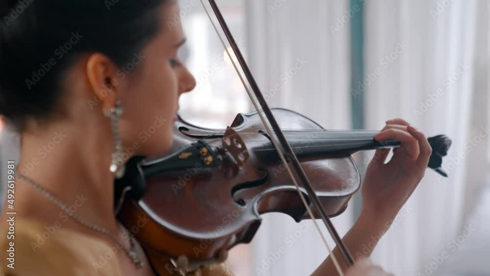 A Young Girl And Man Plays The Violin In A Beautiful Retro Room With Flowers And A Piano. A Young Girl And Man Plays The Violin In A Beautiful Retro Room With Flowers And A Piano.