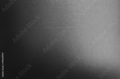 luxury black leather texture background showing grain and a shaft of light across. gradient black artificial leatherette texture use as background, close up view, with blank space for design. photo