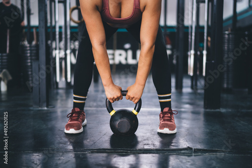 Cropped female athlete holding kettlebell weightlifting in gym studio - endurance and effort on sportive practice,unrecognizable woman with barbell exercising and training for keeping muscles in tonus © BullRun