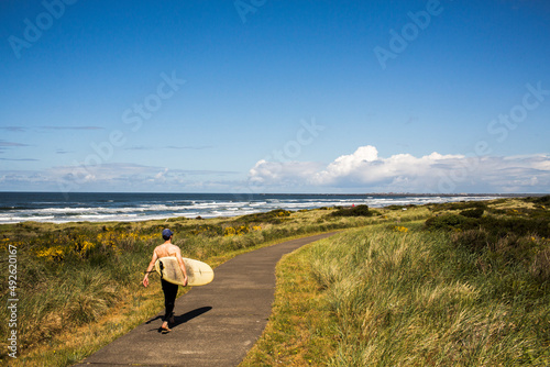 A man carrying a surfboard walks down a path toward the beach photo