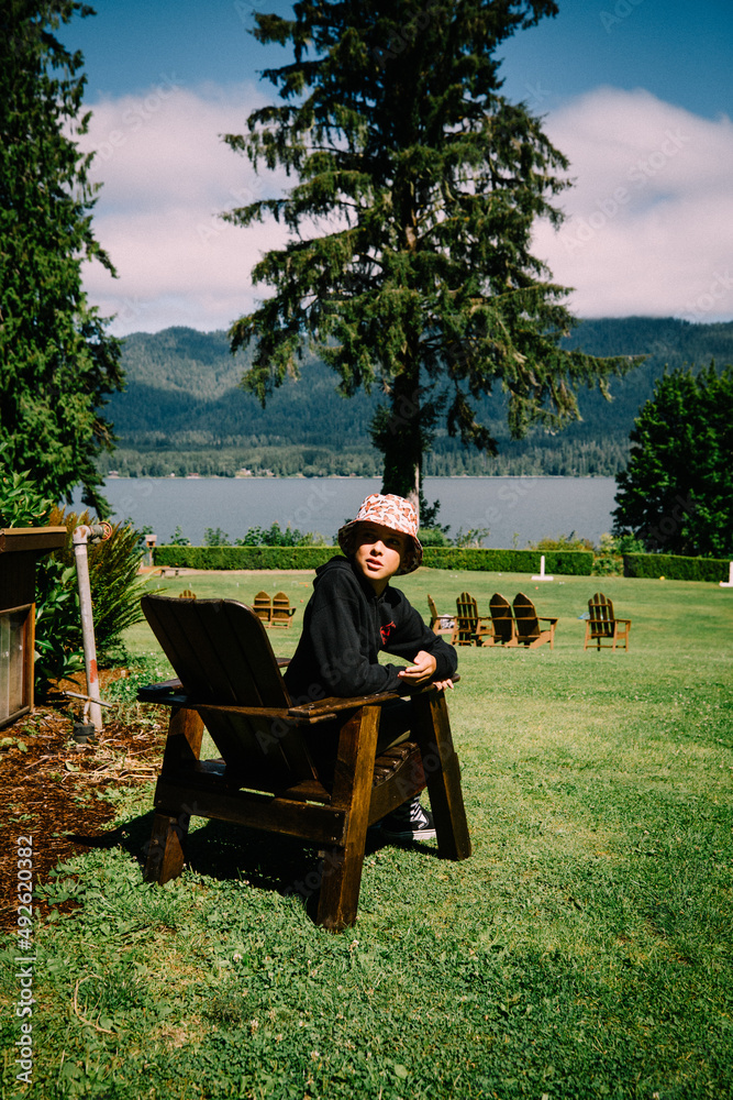 Teen Boy Looks Over Should from Adirondack Chair Next to Lake Teen Boy Looks Over Should from Adirondack Chair Next to Lake