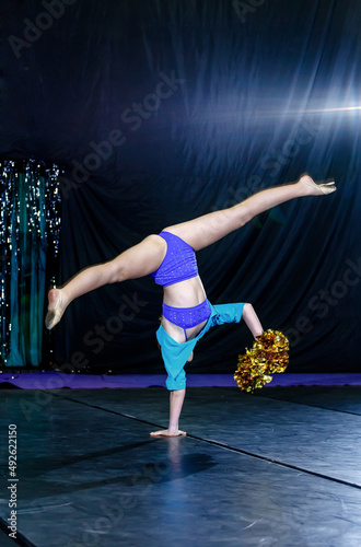 cheerleader girl stands on one hand, pom-poms in the other hand, legs apart