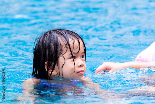 Portrait cute Asian child girl playing in clear blue pool. Children enjoy exercising in water. Kid 4 year old is wet.