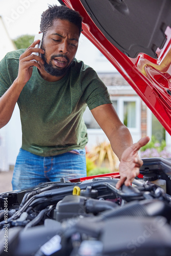 Bild auf Leinwand Man Looking At Engine After Car Breakdown Calling Auto Recovery On Mobile Phone