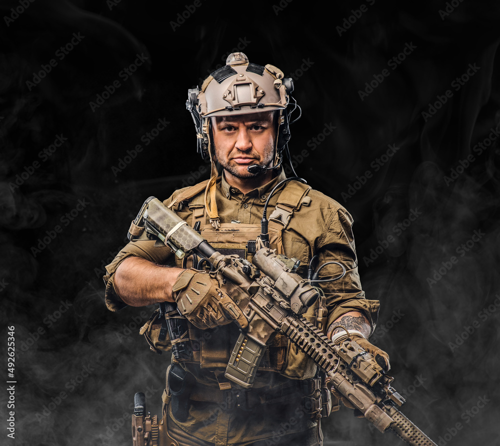 Combative soldier with serious face holding rifle against black background Combative soldier with serious face holding rifle against black background