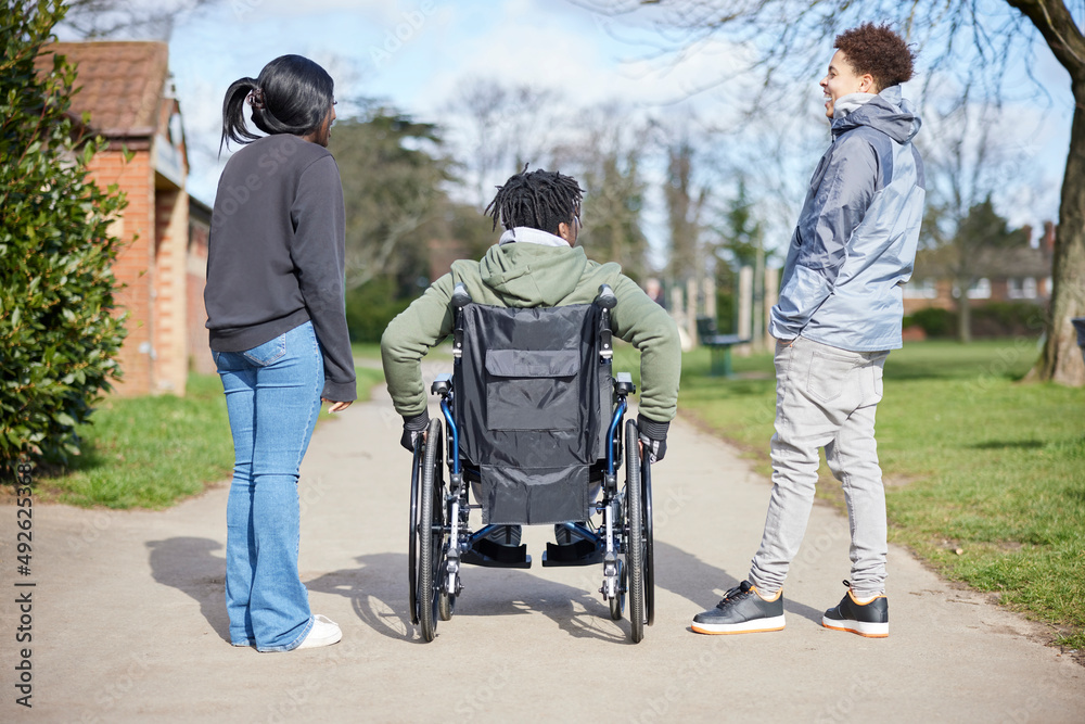 Teenage Boy In Wheelchair Hanging Out Talking And Laughing With Friends In Park Teenage Boy In Wheelchair Hanging Out Talking And Laughing With Friends In Park