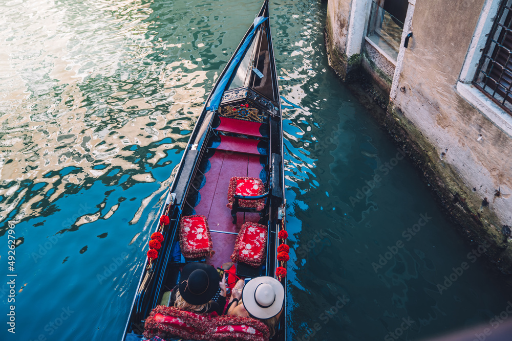 Top view on female tourists enjoying water excursion on gondola during romantic vacations in Venice, unrecognizable women in hats discussing summer trip and sightseeing during free daytime