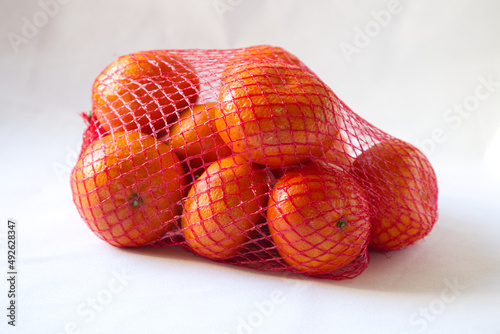 a group of tropical fruit orange mandarin, clementine, tangerine in a red mesh bag packing on white background.