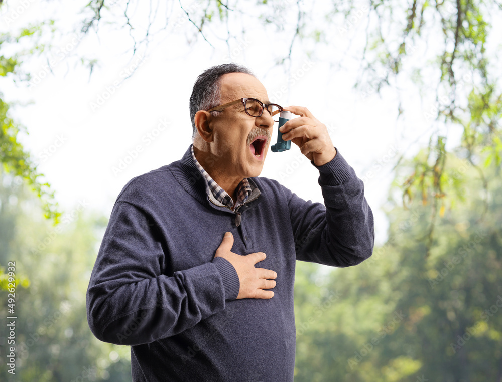 Mature man using an inhaler outdoors Mature man using an inhaler outdoors