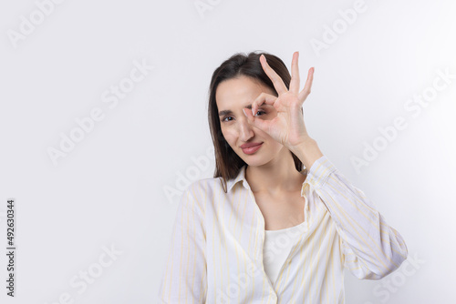 Close up portrait of attractive quirky young woman making binoculars with hands showing ok gesture on white studio background.