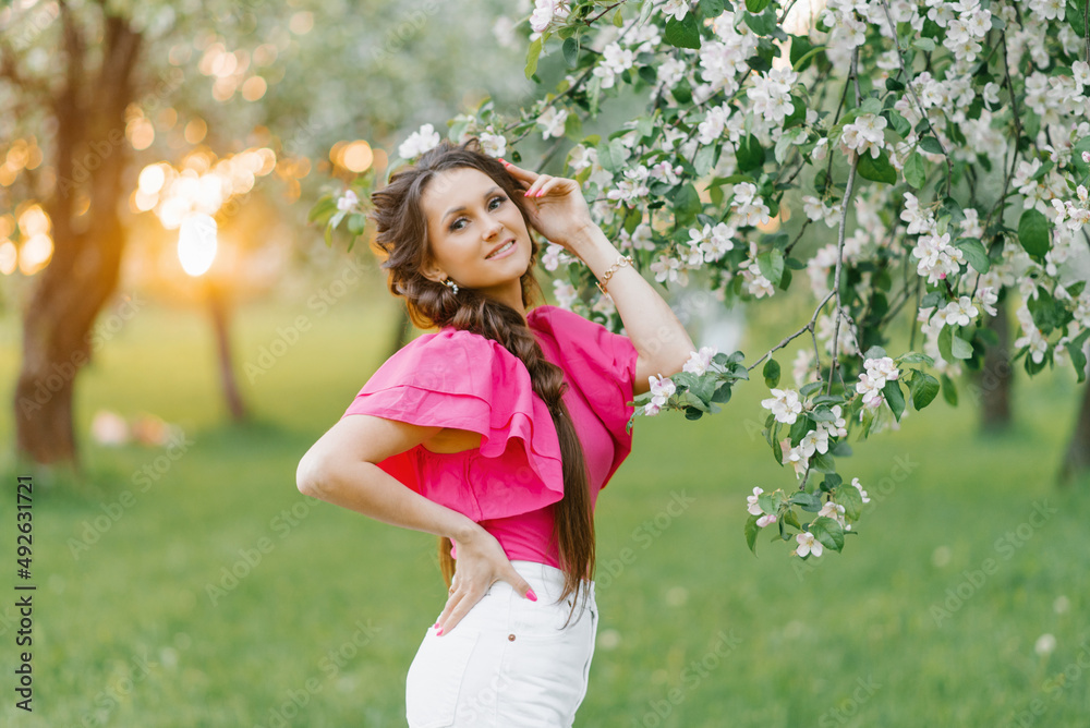 A beautiful young European woman with beautiful makeup and braids in spring in the park, in a blooming apple orchard A beautiful young European woman with beautiful makeup and braids in spring in the park, in a blooming apple orchard