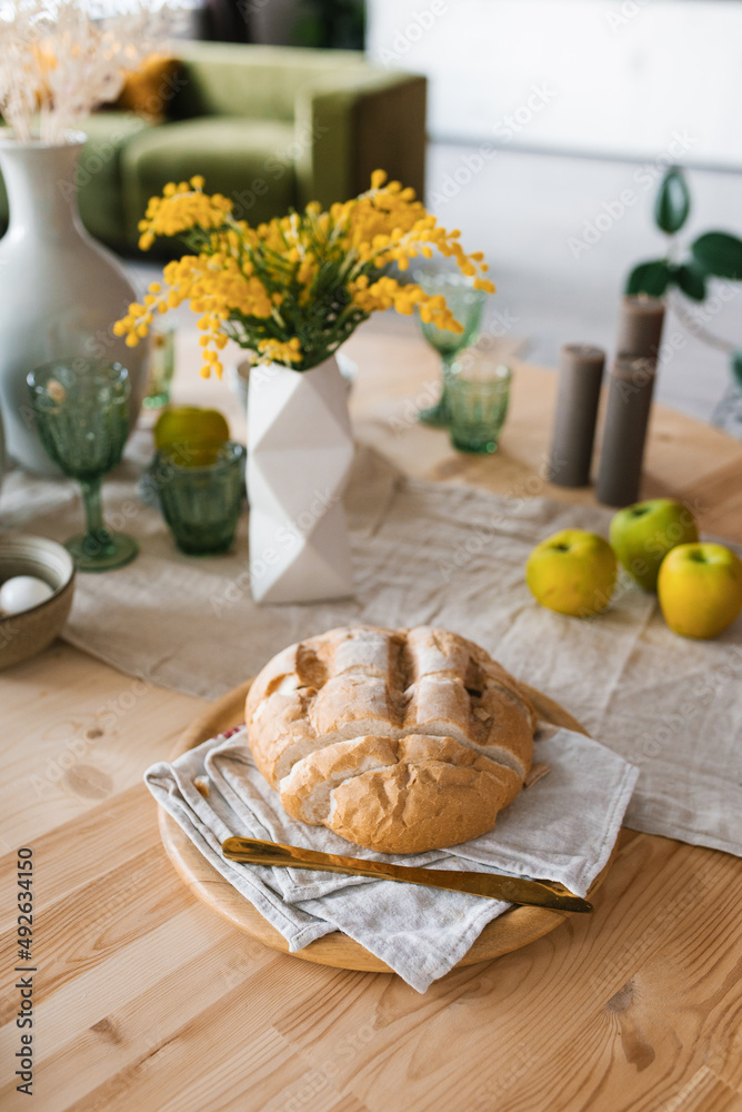 A loaf of fresh bread on the breakfast table, mimosa flowers in a vase A loaf of fresh bread on the breakfast table, mimosa flowers in a vase
