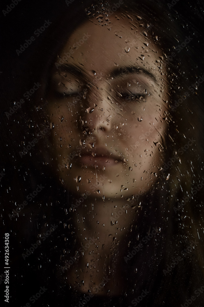 Portrait of a beautiful young long haired woman with closed eyes behind a glass plate covered with droplets, focus on the droplets Portrait of a beautiful young long haired woman with closed eyes behind a glass plate covered with droplets, focus on the droplets