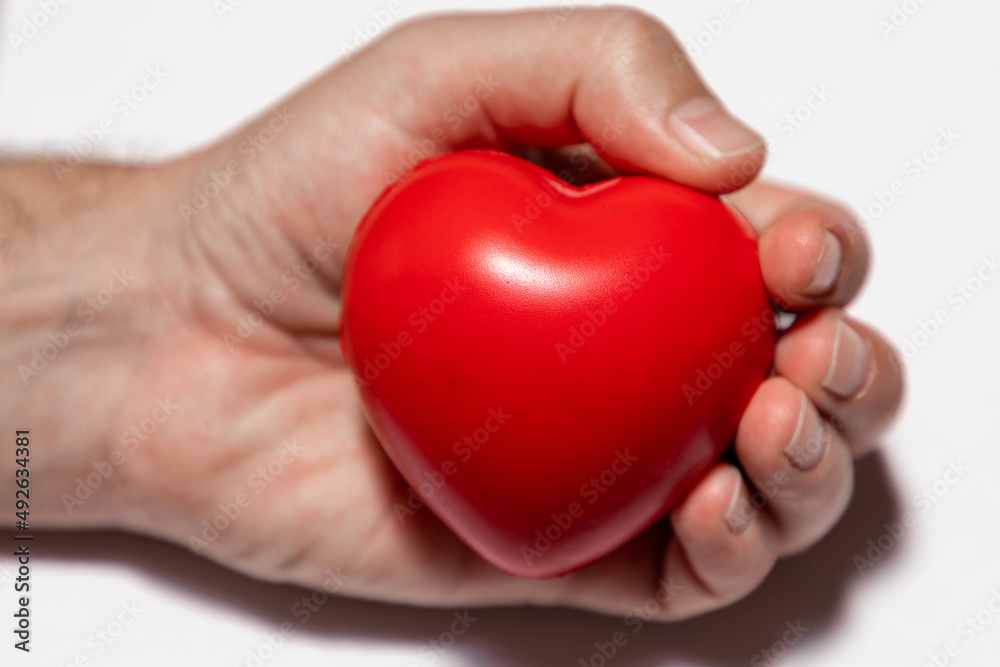 Selective focus on a red heart in a caucasian hand on a white background.  The hand is out of focus. 