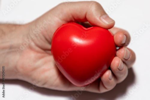 Fototapeta Naklejka Na Ścianę i Meble -  Selective focus on a red heart in a caucasian hand on a white background.  The hand is out of focus. 