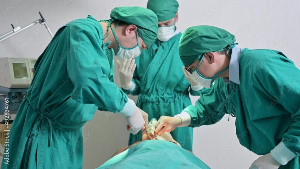 Team of asian surgeons in surgical gown performing surgery a seriously injured patient in operating room at hospital Team of asian surgeons in surgical gown performing surgery a seriously injured patient in operating room at hospital