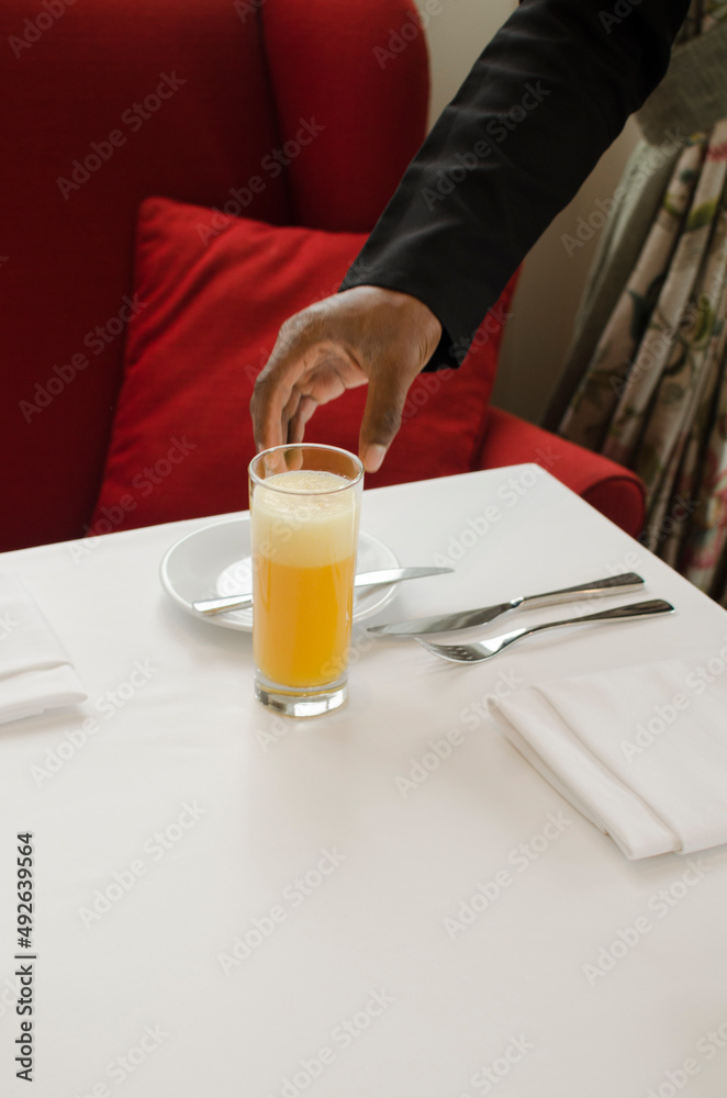 waiter holding glass of orange juice with hand on a restaurant table waiter holding glass of orange juice with hand on a restaurant table