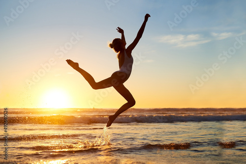 Youre free to be whoever. Shot of a young woman jumping into mid air against a beautiful sunset at the beach.