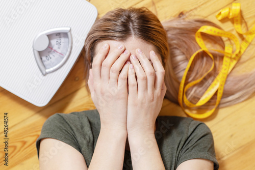 Fotografie Upset and sad woman covering face with hands while lying on wooden floor with wh