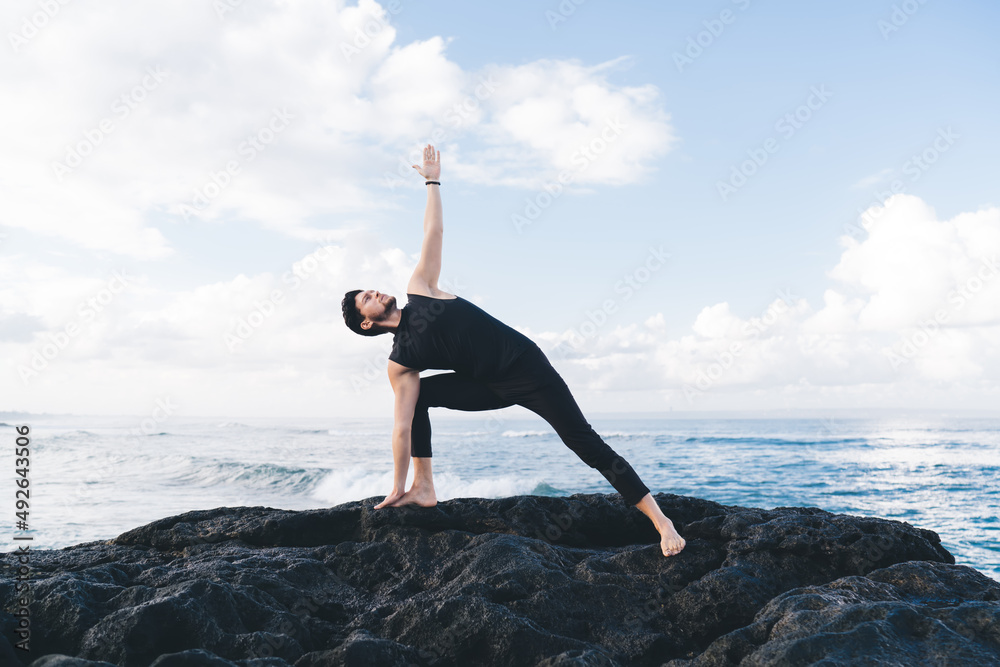 Calm male in sportive wear standing in yoga pose and meditate during morning mindfulness concentration at coastline seashore, Caucasian man enjoying hatha practice for enlightenment harmony Calm male in sportive wear standing in yoga pose and meditate during morning mindfulness concentration at coastline seashore, Caucasian man enjoying hatha practice for enlightenment harmony