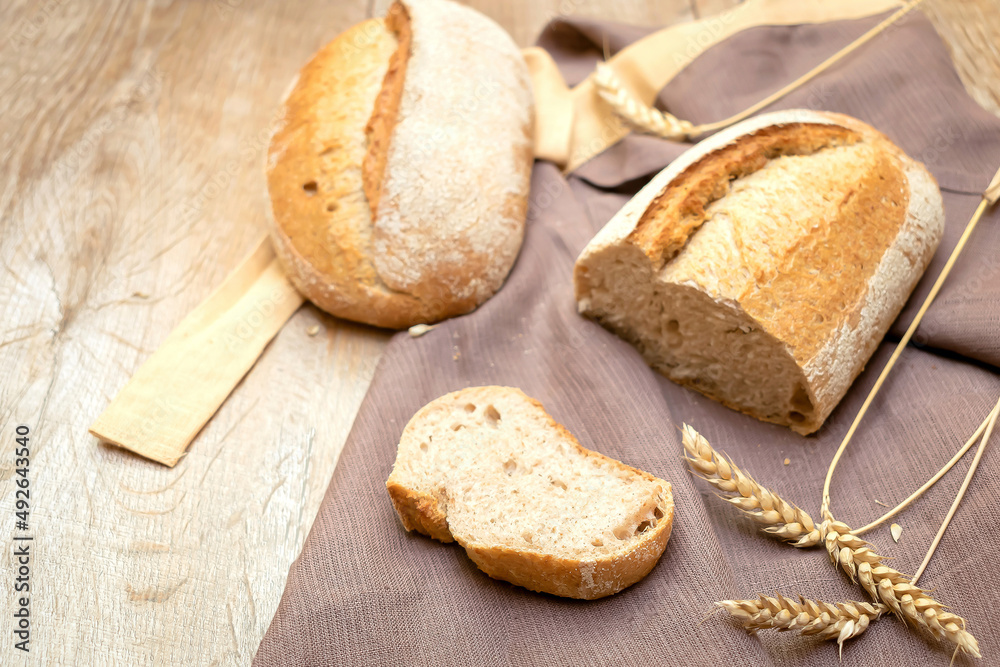 loaf of fresh bread and cutted slice of baguette bun on wooden rustic background with copy space, baked pastry food closeup loaf of fresh bread and cutted slice of baguette bun on wooden rustic background with copy space, baked pastry food closeup