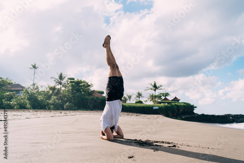 Caucaisan male in active wear doing exercises at coastline beach recreating and keeping body shape, strong man have morning hatha yoga near ocean enjoying time for meditation and concentration
