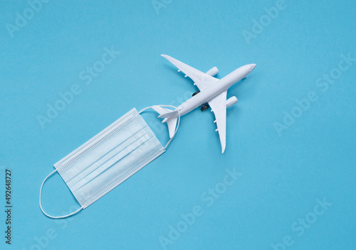 a white plane with a medical mask on a blue background. the concept of social distance. travel planning.