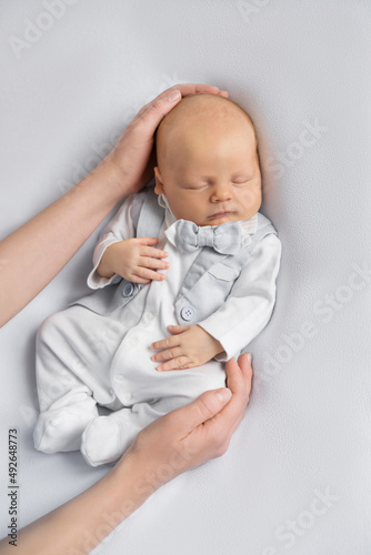 mom's hands hold newborn baby boy in a suit sleeping on a  light background. Happy pregnancy and childbirth. Children's theme. Top view