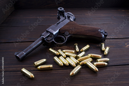 Fotografija Historic Luger P08 Parabellum handgun and shiny 9 mm bullets on wooden vintage b