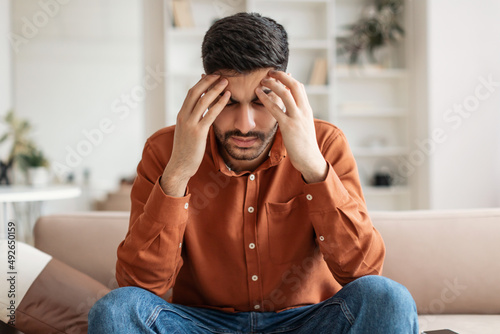 Stressed Arab man sitting on couch and thinking © Prostock-studio