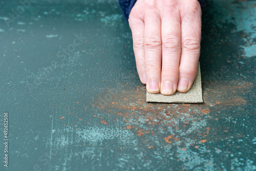 Manos con papel de lija quitando el óxido de una superficie metálica