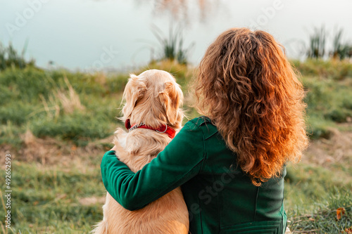 Golden retriever dog with a curly woman walking outdoors on sunny day. Training the dog in the park. love and care for the pet. Back view