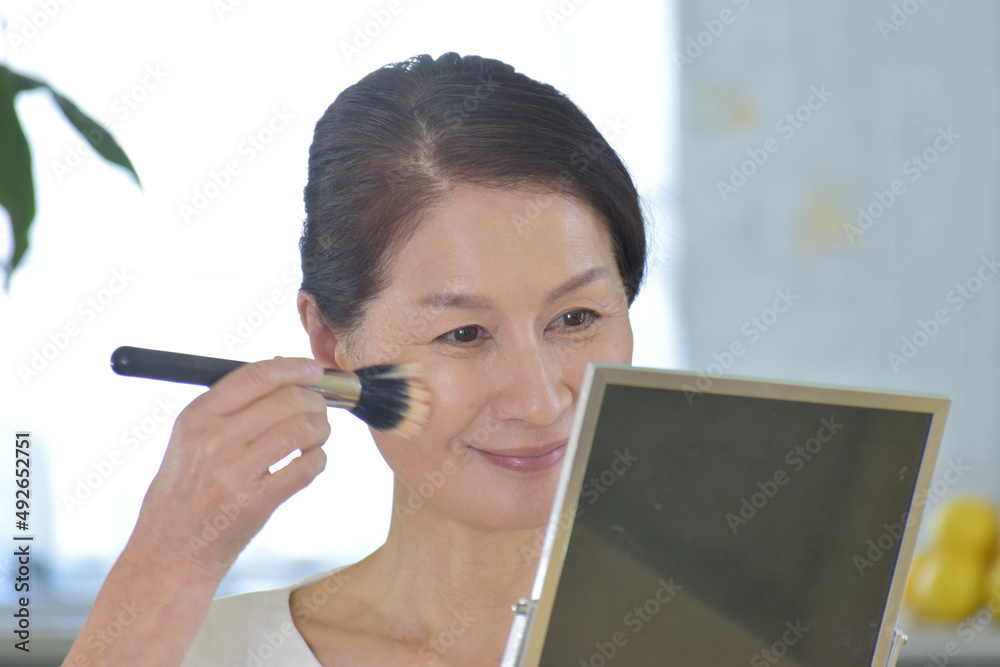 鏡を見ながらパウダーをはけではたく60代女性 鏡を見ながらパウダーをはけではたく60代女性