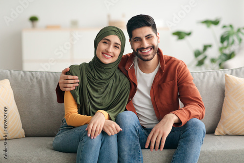 Middle Eastern Couple Hugging Sitting On Sofa Smiling At Home