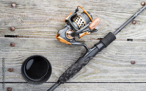 Fishing rod, spinning reel and cup of hot coffee on the wooden background pier river bank. Sunrise. Misty fog against the backdrop of lake. The concept of rural getaway. Article about fishing day.
