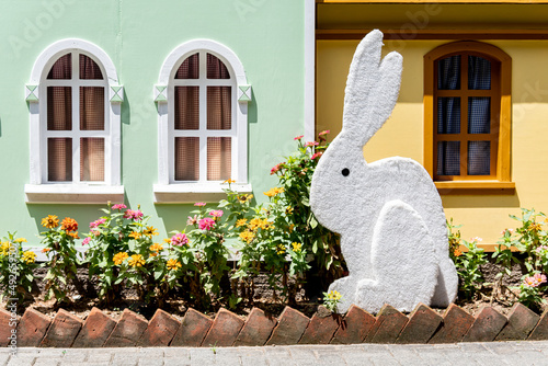 Coelho da páscoa em frente a casa verde com jardim florido