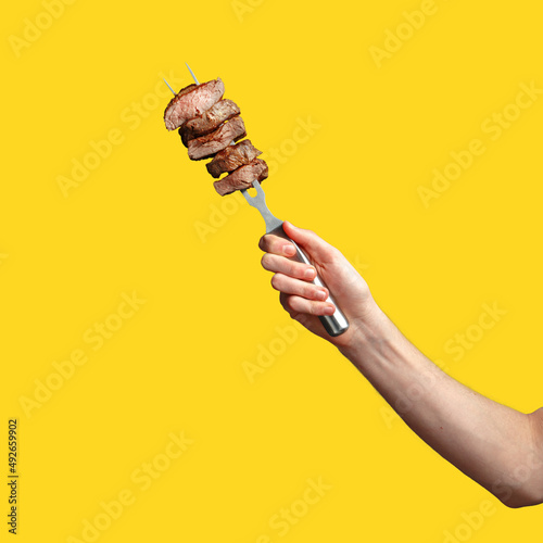 a man's hand holds pieces of roasted meat on a fork